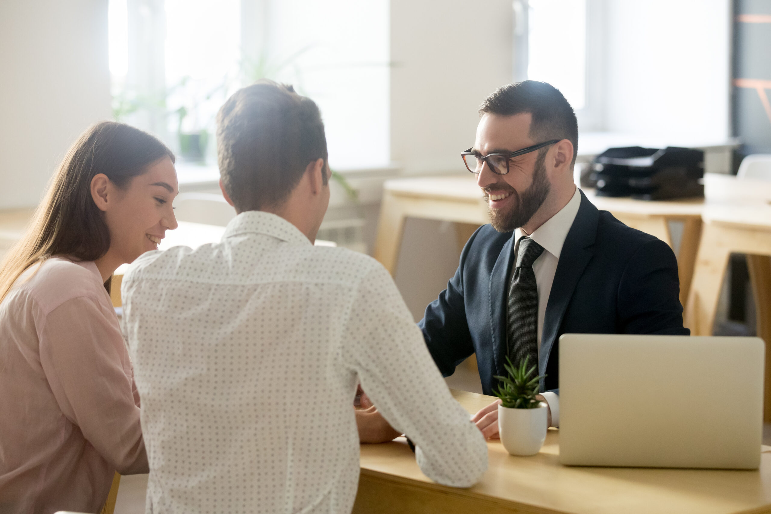 A couple meeting with a professional advisor in an office setting, with a laptop on the table.