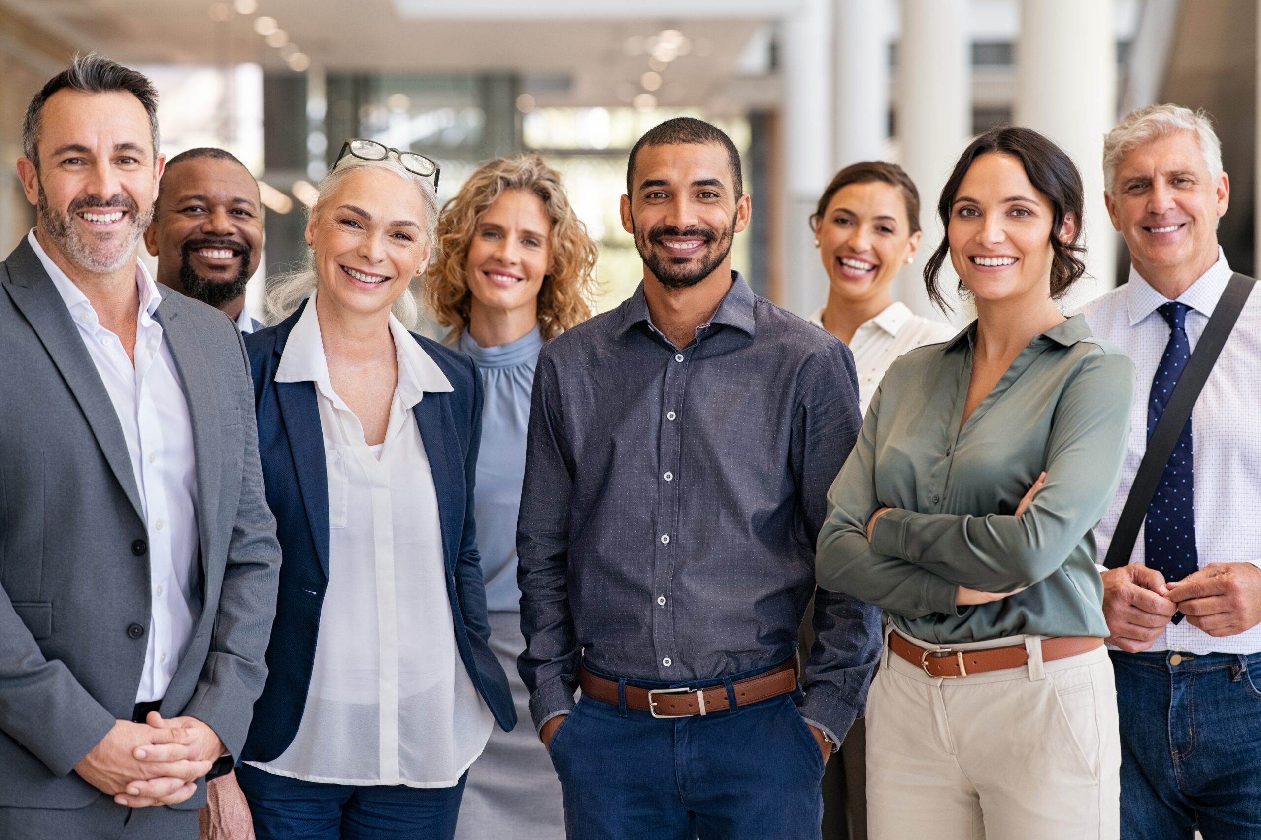 Diverse group of professionals smiling and standing together in a workplace setting.