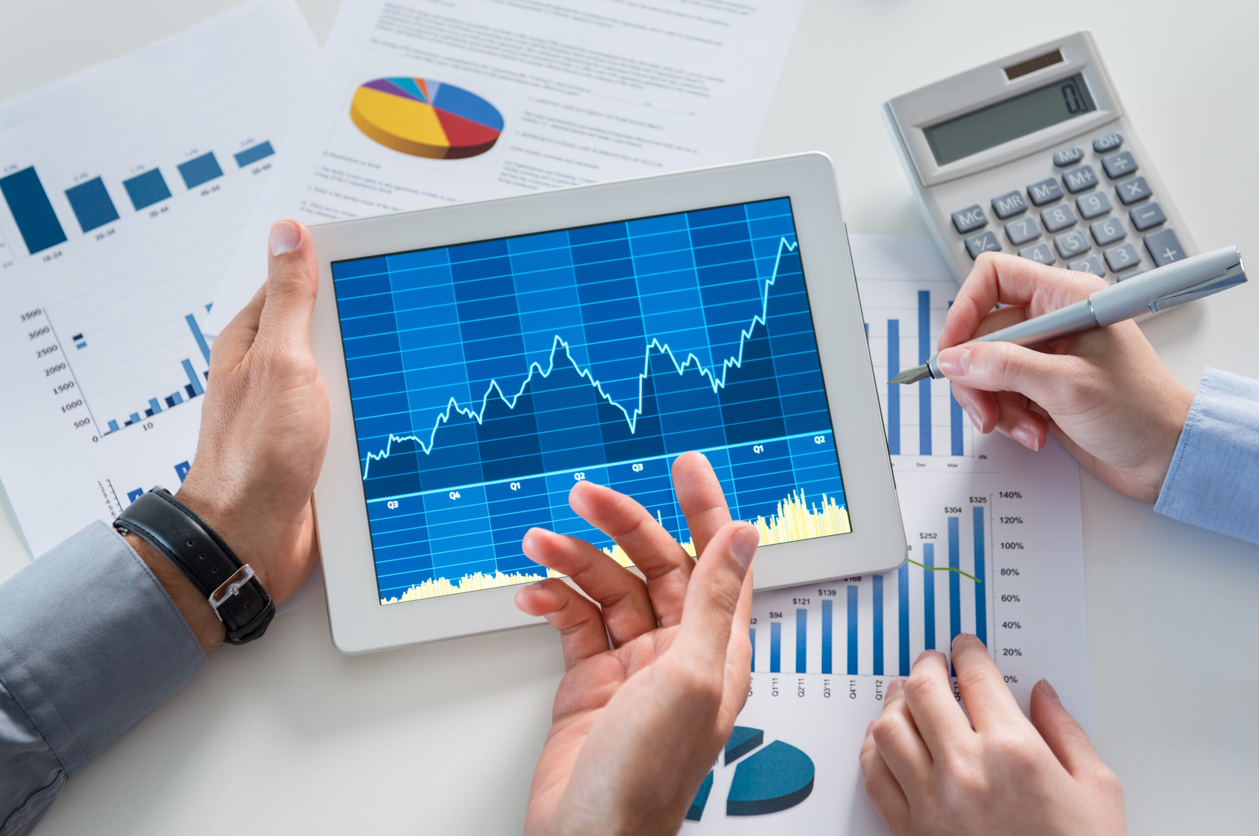 Tablet displaying financial data with a growth chart, surrounded by hands analyzing graphs and reports.